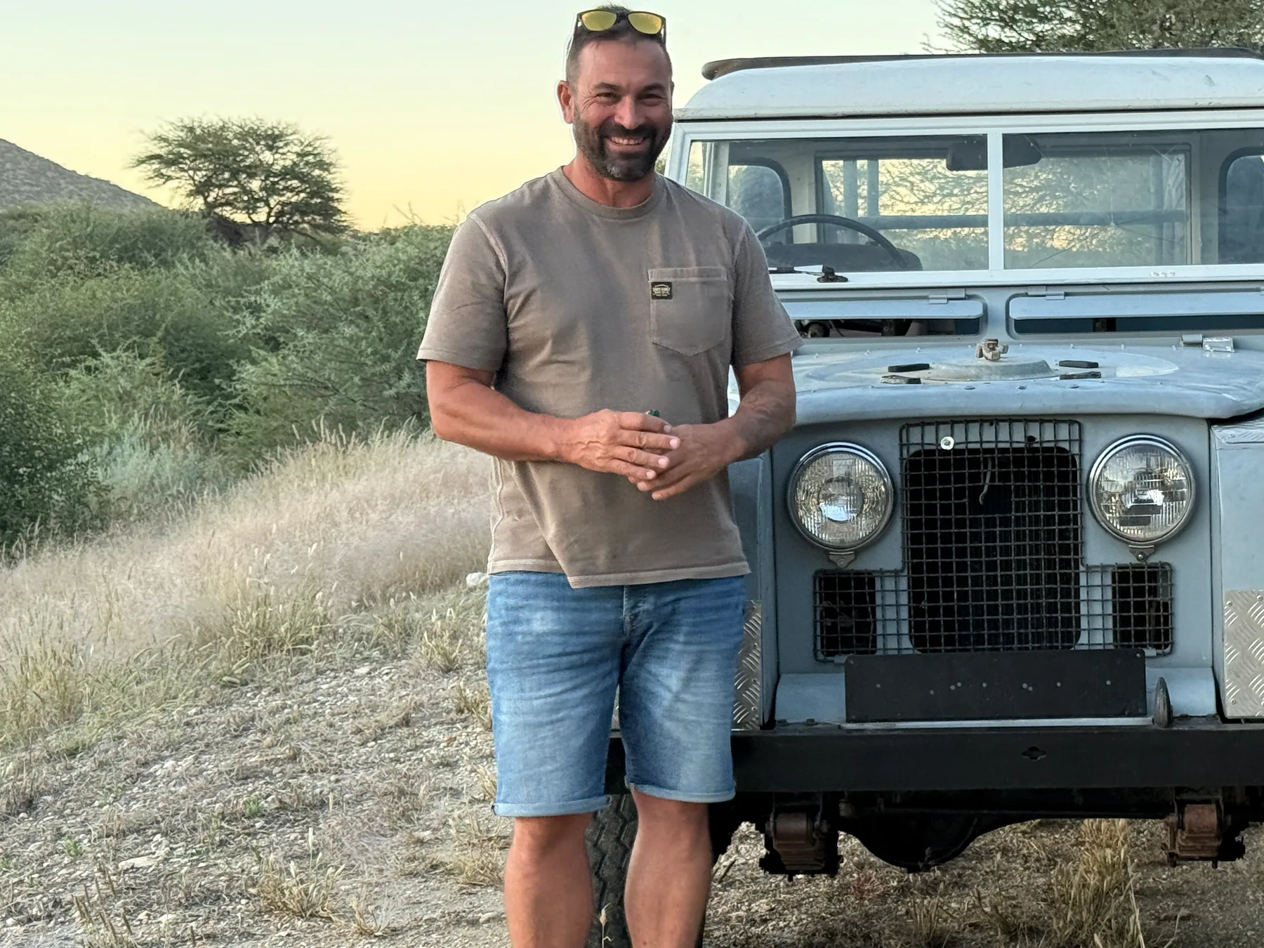 Chris Sandmann, owner of Namvic Safaris, standing in front of a Namvic safari vehicle at sunset